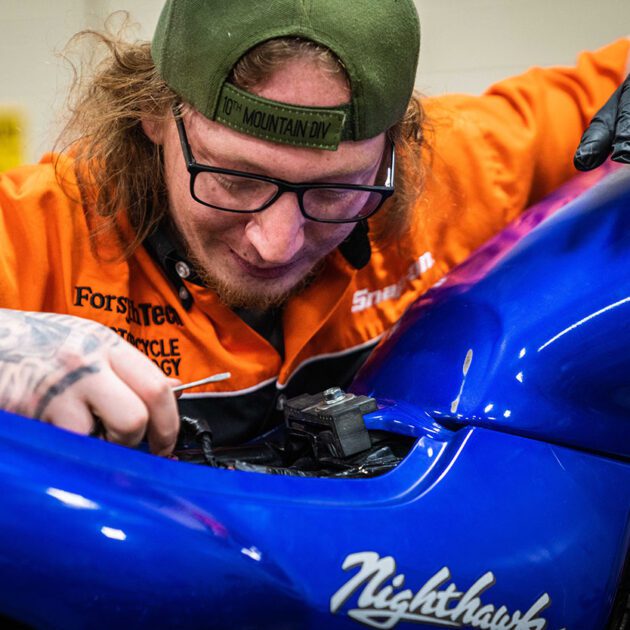 Motorcycle Mechanics student inspecting electronics underneath the seat of a Honda motorcycle.