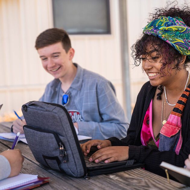 image of early college students sitting on bench outside working on laptops