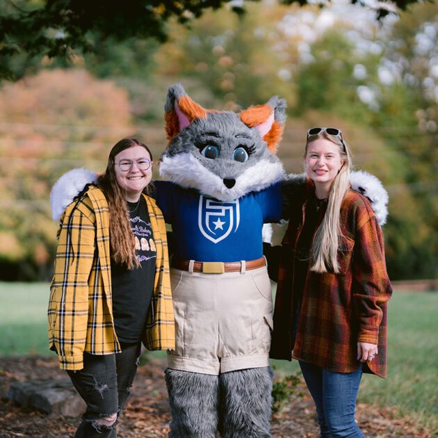 image of two students standing alongside mascot blaze