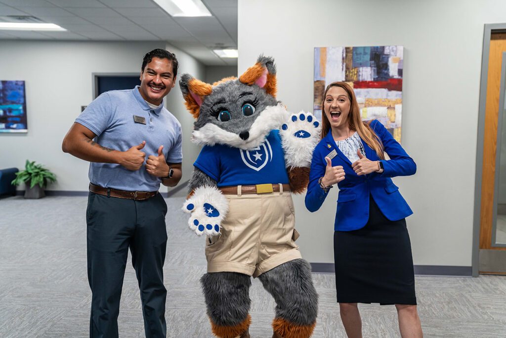 two students pose alongside mascot blaze indoors