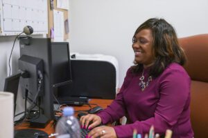 Black woman in a purple top typing on a computer