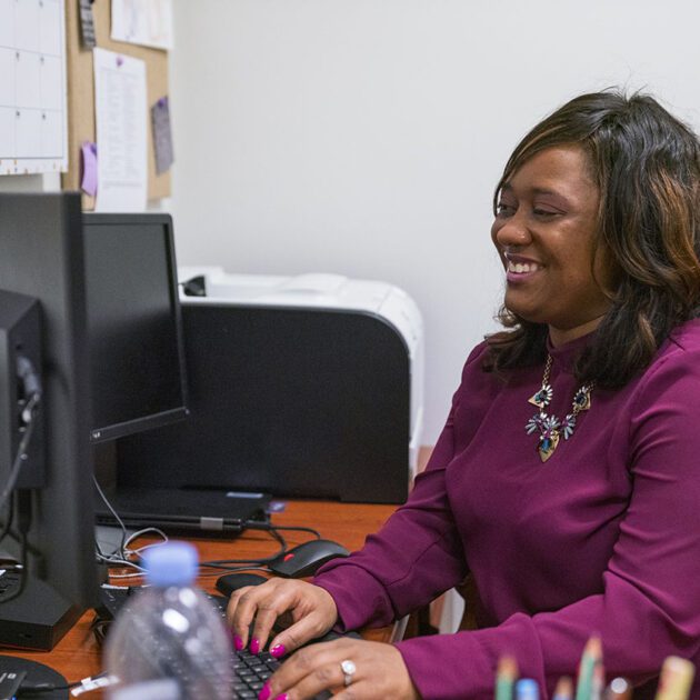 Black woman in a purple top typing on a computer