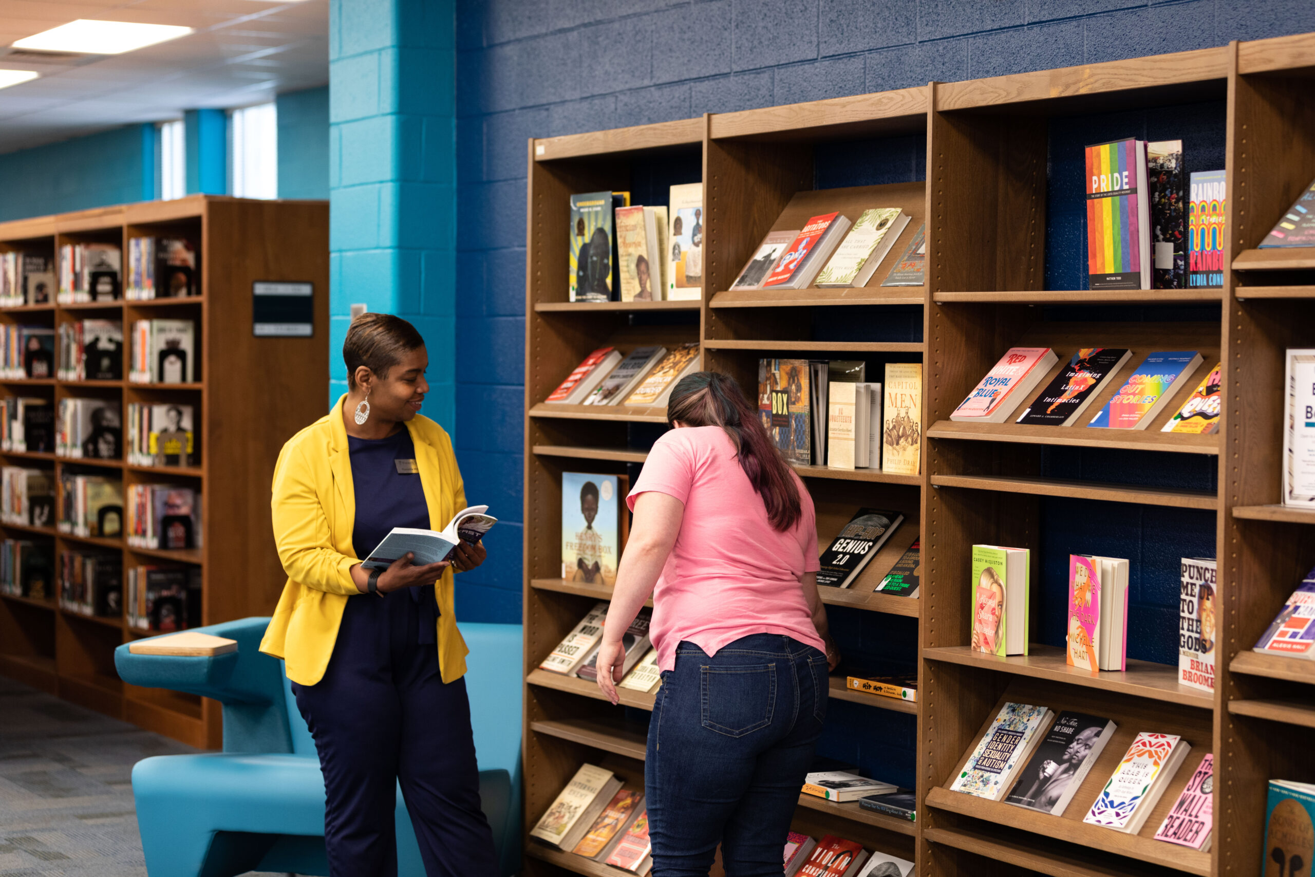 A Librarian helping a student pick out a book from the shelf.