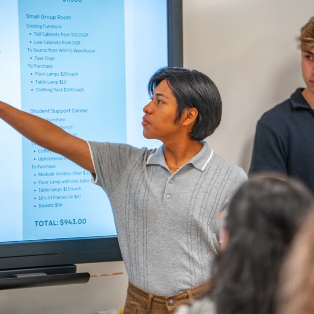 A young male student points at a screen.