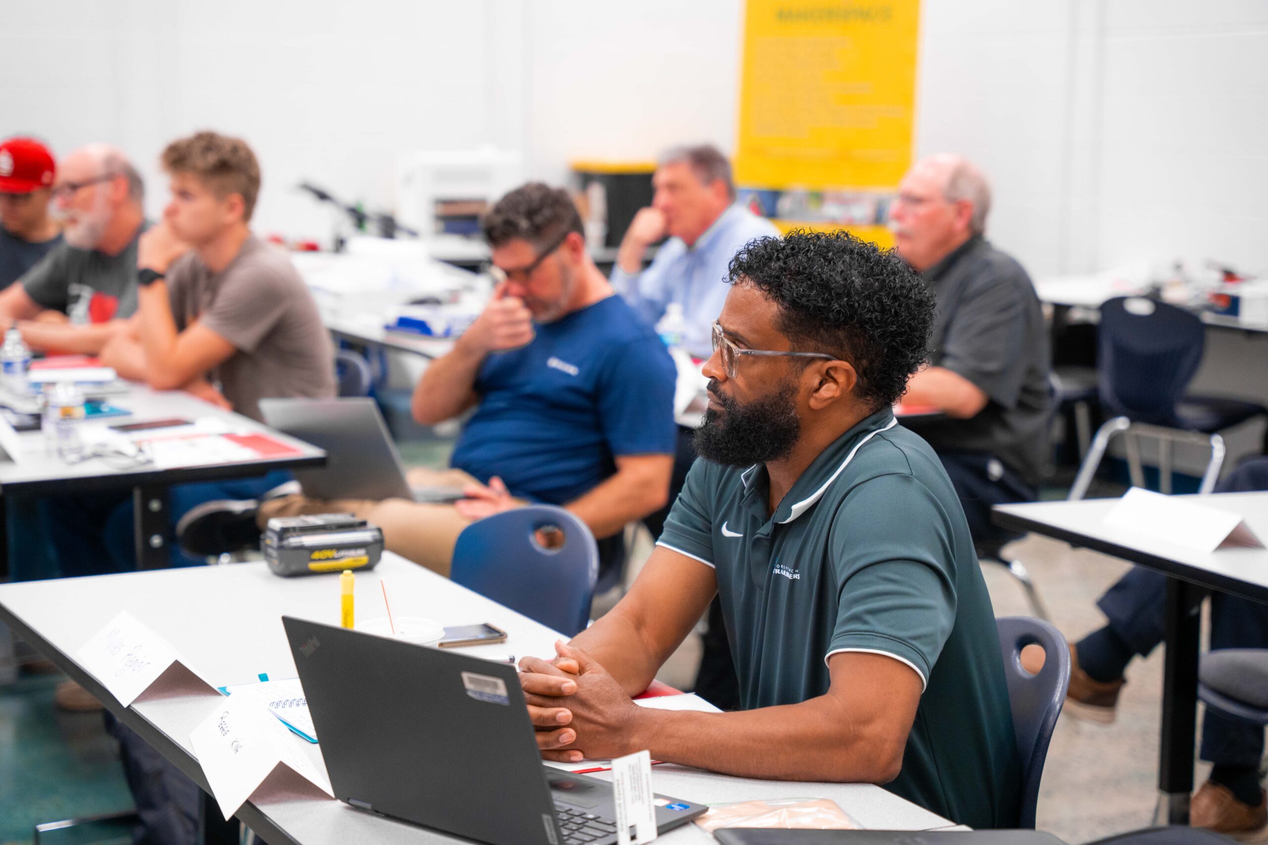 Men of different ages and races sit in a classroom with their eyes focused forward. 