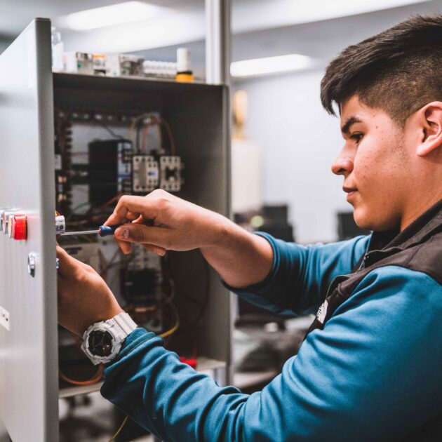 A student works on an electrical control panel, using a screwdriver to adjust wiring and components during a hands-on mechatronics lab at Forsyth Tech.